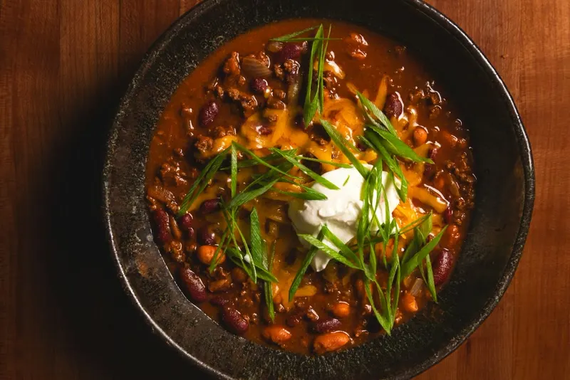 A bowl of chili with kidney beans, cheddar, sour cream and scallions