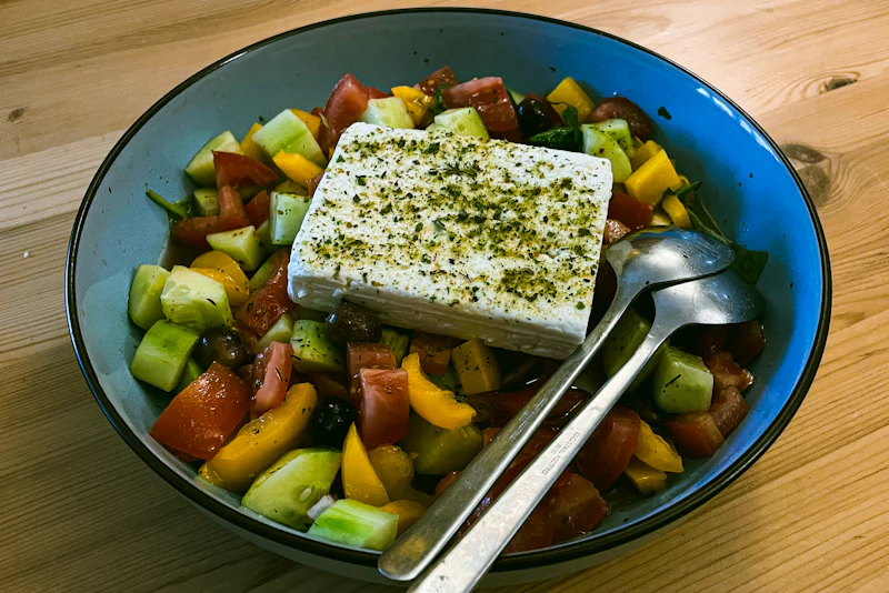 A Greek salad topped with a block of feta and oregano